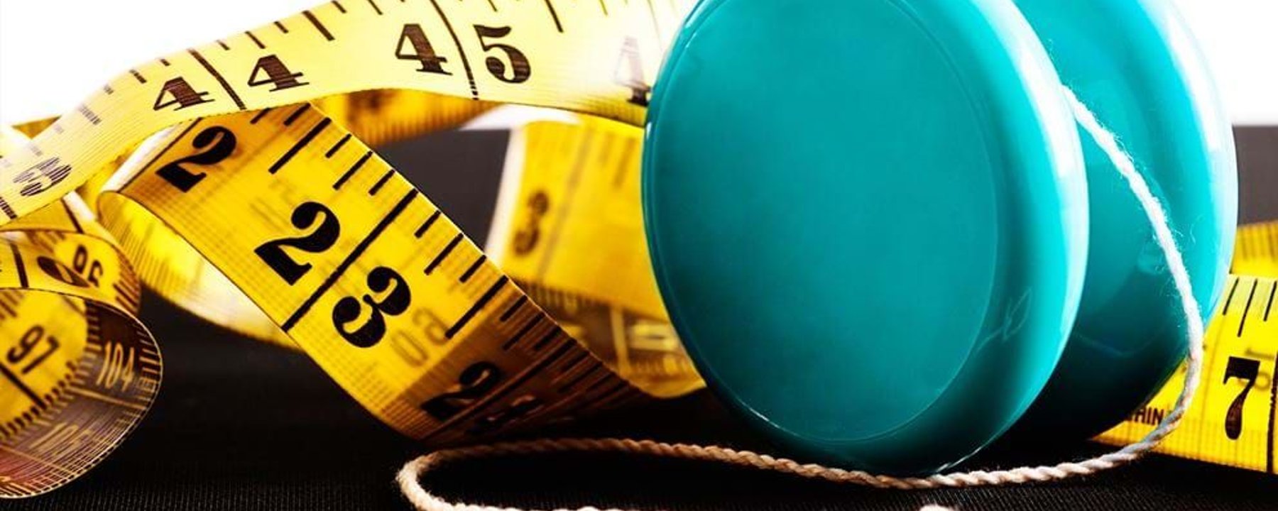Blue yo-yo with white string next to a yellow measuring tape on black surface