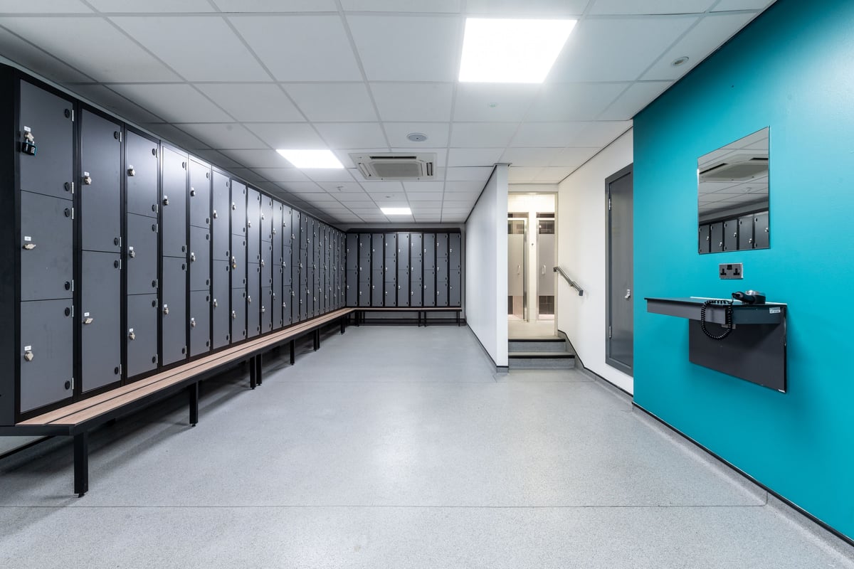 PureGym Harrogate: Rows of lockers, benches, and a sanitation station in a tiled corridor.