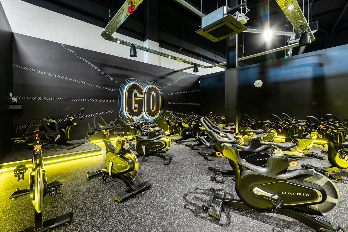 PureGym Stockton-on-tees Teesside Park: Rows of stationary cycling bikes and free weights in a dimly lit studio interior.