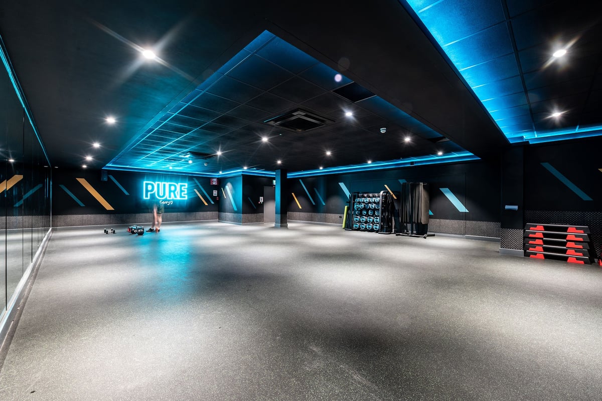 PureGym Epsom: Rubberized floor, neon-lit studio space with weight racks and functional training area.