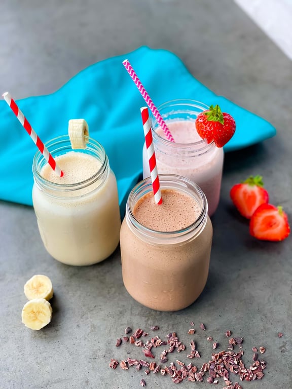 Three jars of banana, strawberry, and chocolate smoothies with matching straws