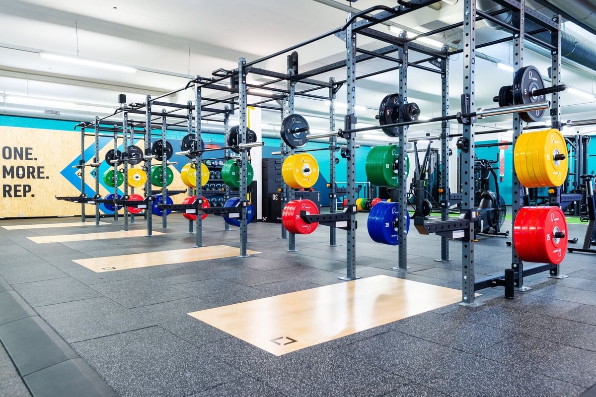 PureGym Dübendorf: Weights room with squat racks and colourful weight plates on racks.