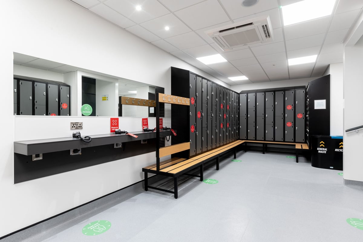 PureGym Colchester Retail Park: Rows of lockers, benches, and open space with floor markings for physical activities.