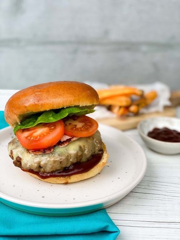 Cheeseburger with lettuce, tomato, and sauce on a white plate with fries and ketchup.