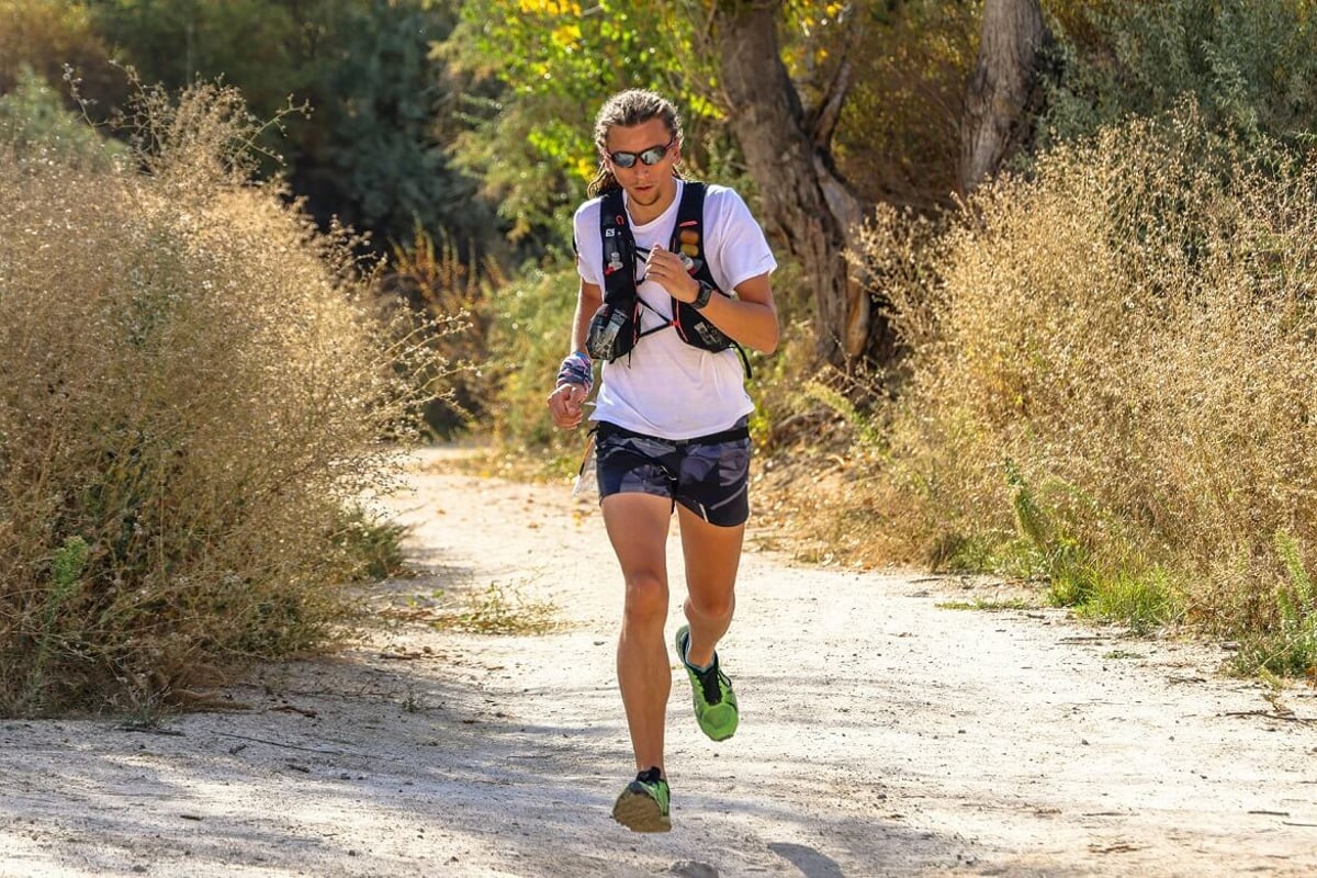 Man running on a dirt path surrounded by dry bushes and trees in daylight