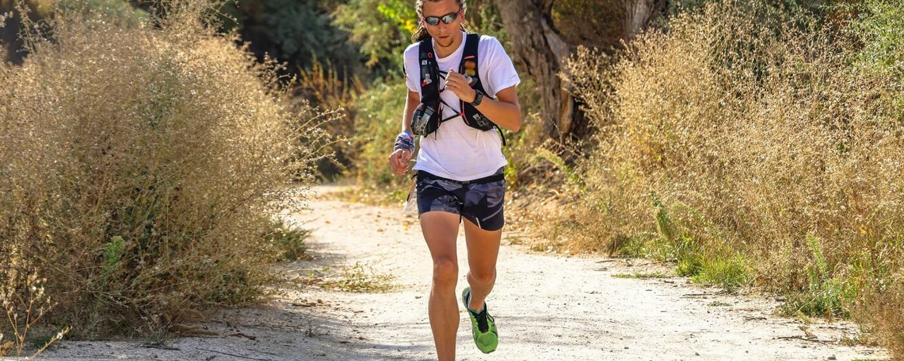 Man running on a dirt path surrounded by dry bushes and trees in daylight