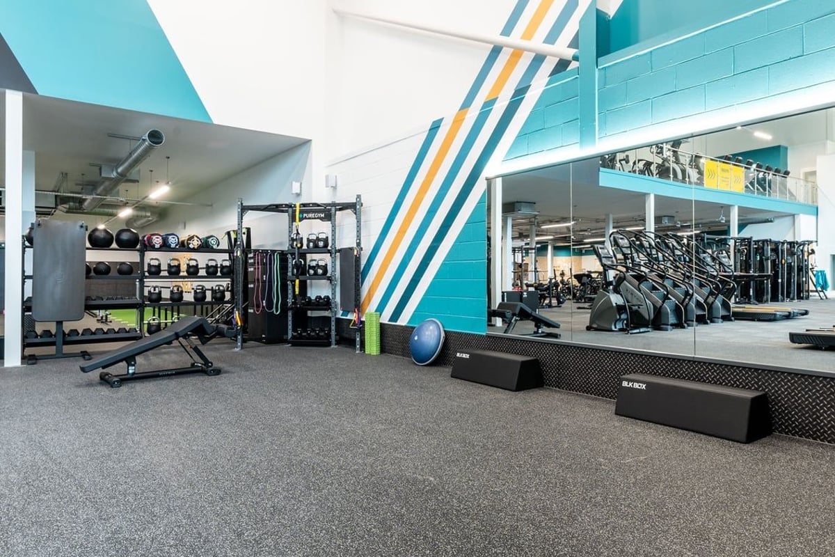 PureGym Caerphilly: Resistance machines, free weights, benches, and rubberized flooring in a brightly colored gym space.