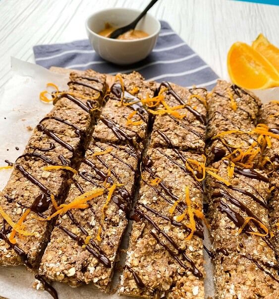 Oat bars drizzled with chocolate and orange zest on parchment with orange slices and sauce