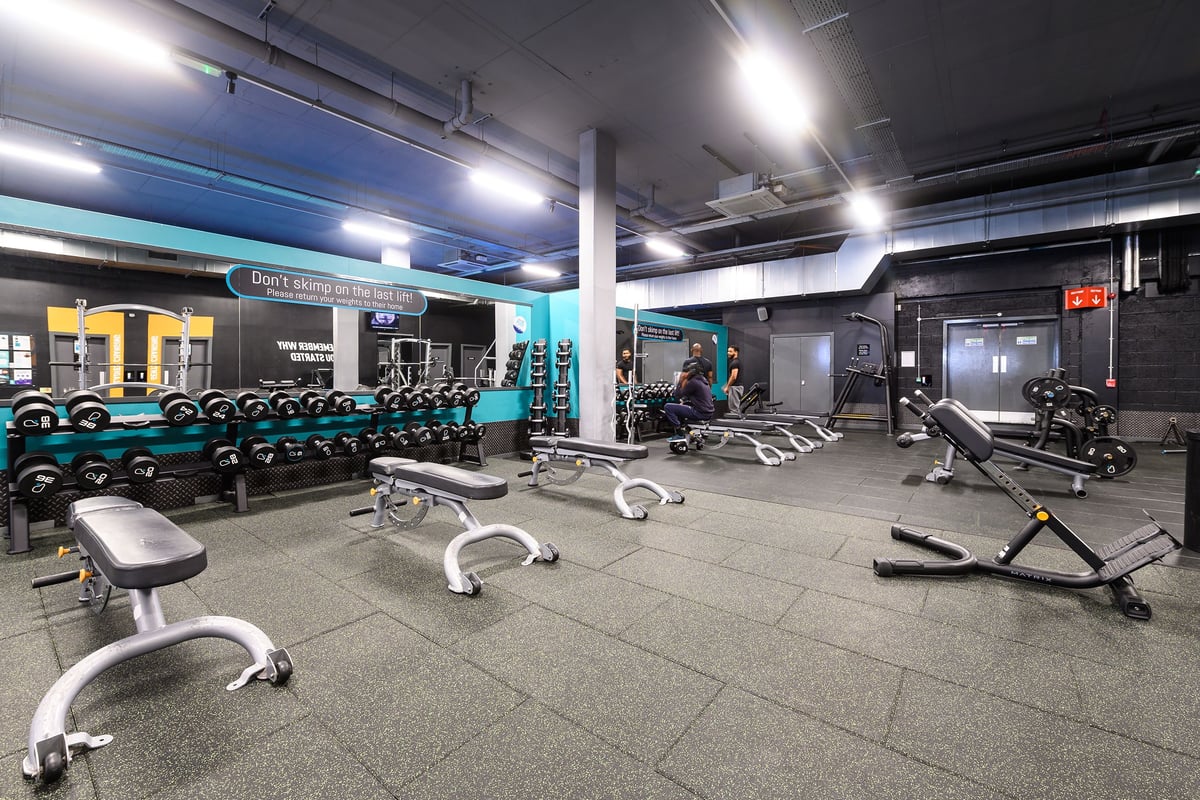 PureGym London Acton: Weightlifting area with free weights, benches, weight machines, and rubberised flooring.