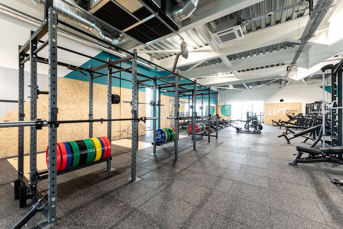 PureGym Bicester: Racks with weight plates, squat stations, benches, and rubberised flooring in a gym facility.
