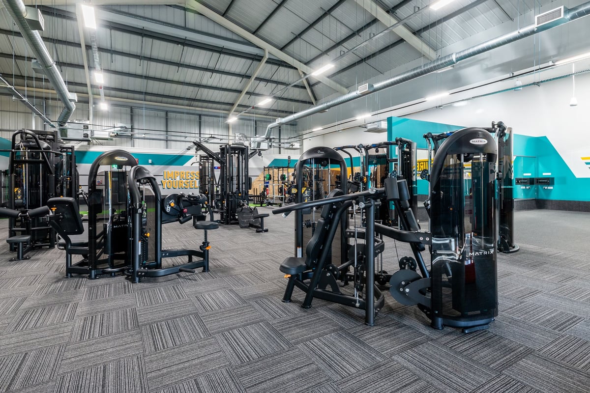 PureGym Oswestry: Fitness studio with resistance machines, cable crossovers, and weight racks on rubberized flooring.
