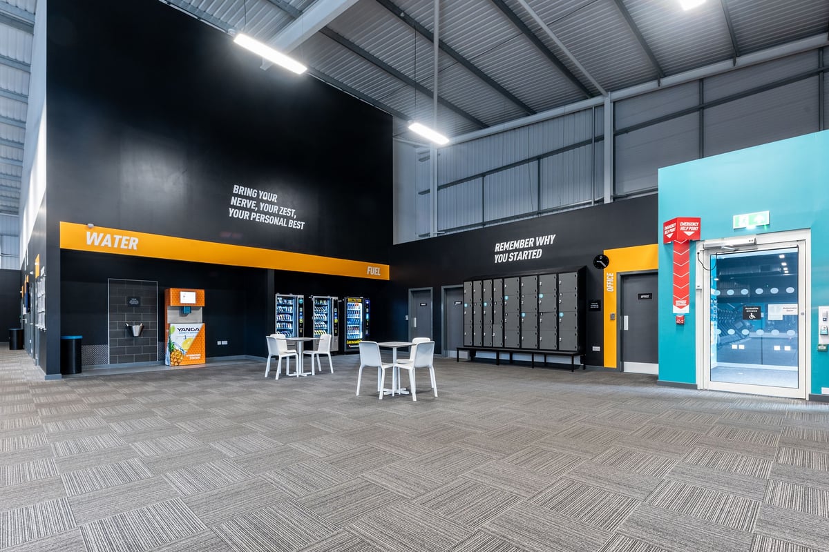 PureGym Widnes: Lockers, vending machines, water, yanga water machine, and tables and chairs in the gym's welcome foyer.