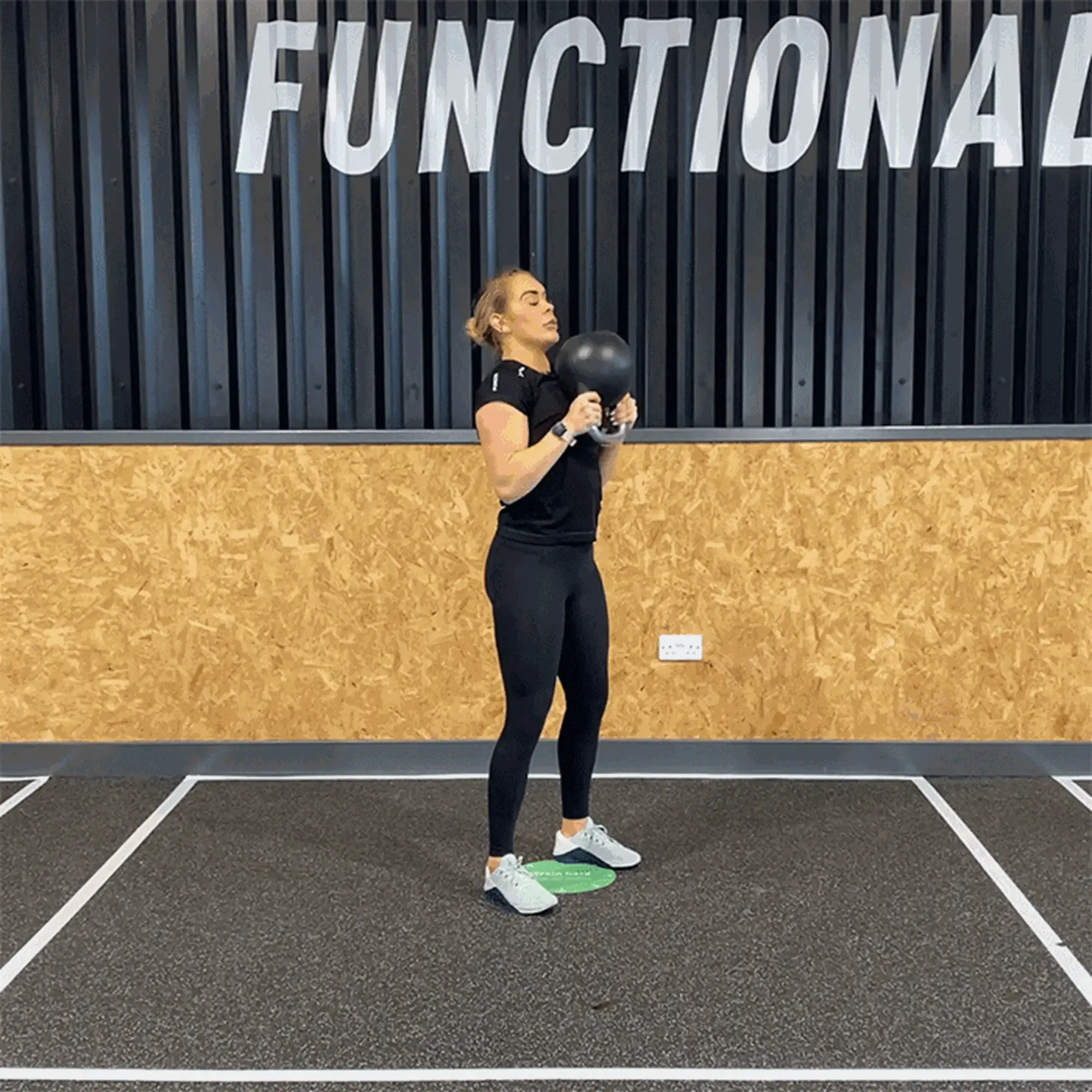 Woman in black workout clothes lifting a kettlebell in a gym with FUNCTIONAL sign above