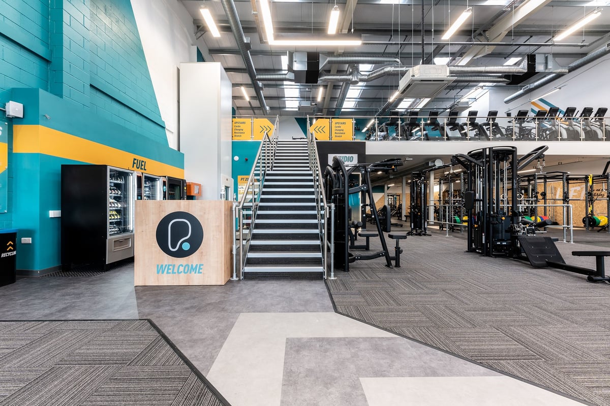 PureGym Consett: Weight racks, resistance machines, staircases, rubberised flooring in a modern gym setup.
