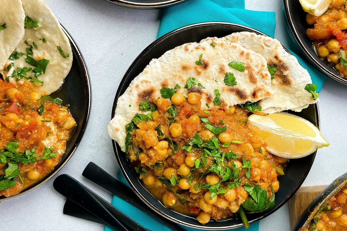 Chickpea curry with fresh coriander served in black bowls with flatbread and lemon wedge
