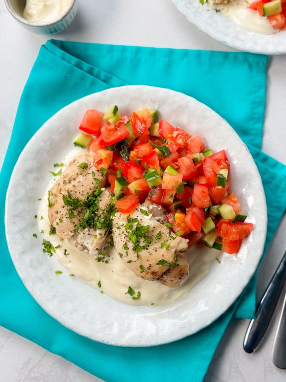 Grilled chicken thighs with chopped tomato and cucumber salad on white sauce on a plate