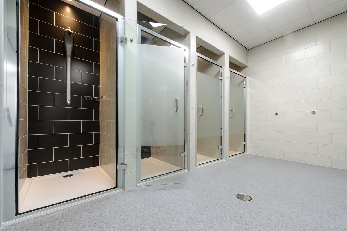 PureGym Leeds Kirkstall Bridge: Glass-enclosed shower stalls, wall tiles, and floor drain.