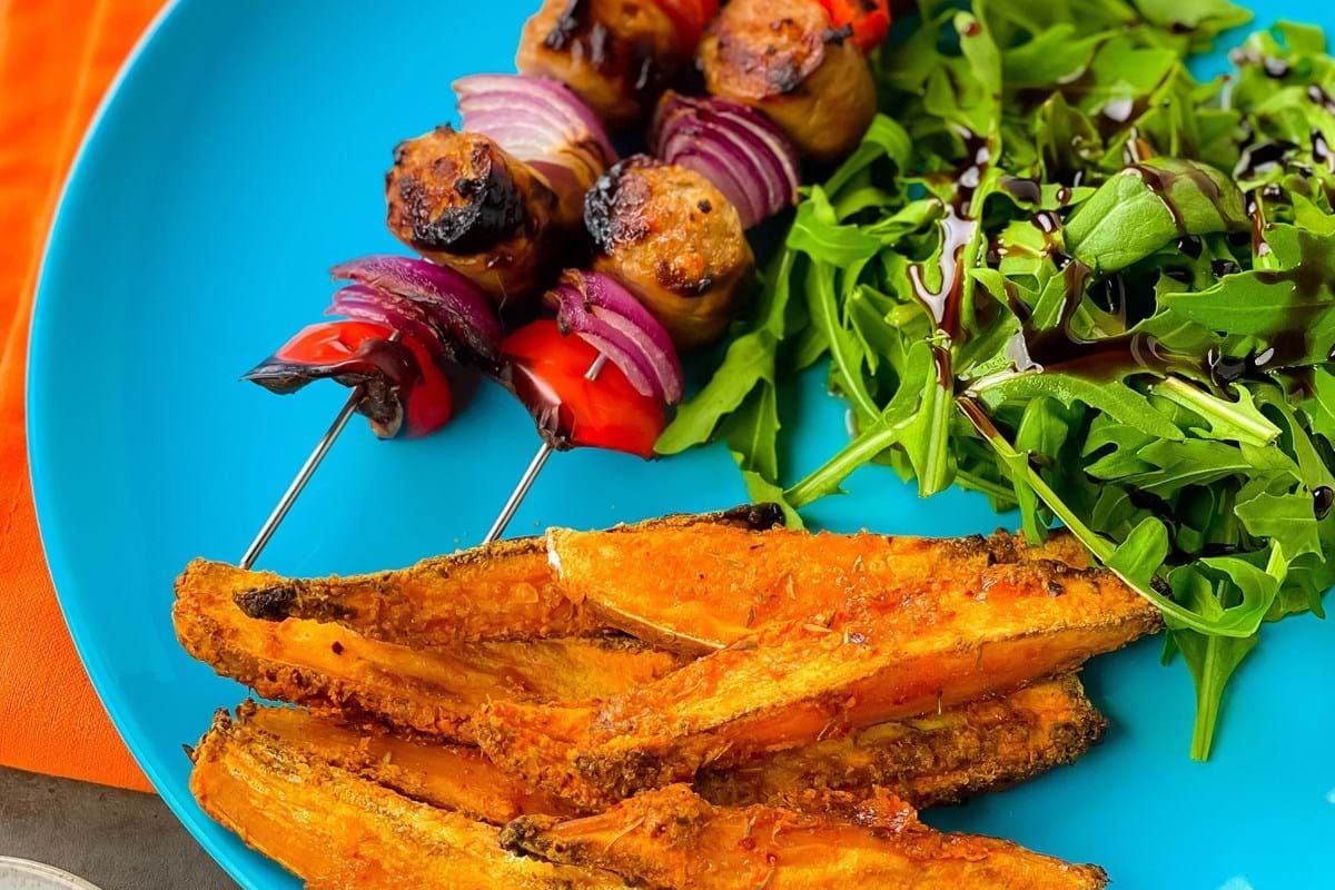 Grilled vegetable skewers with sweet potato fries and salad on a blue plate.