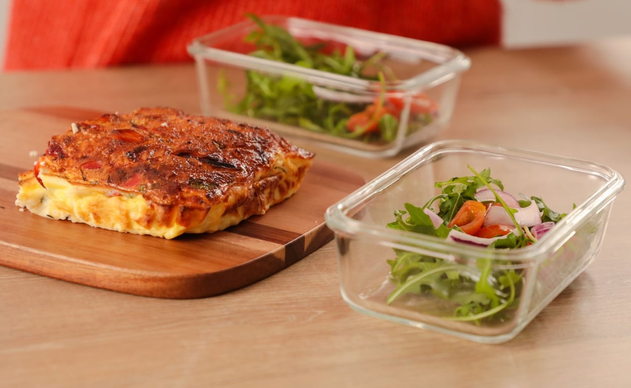 Sweet potato frittata on wooden board with two containers of fresh green salad