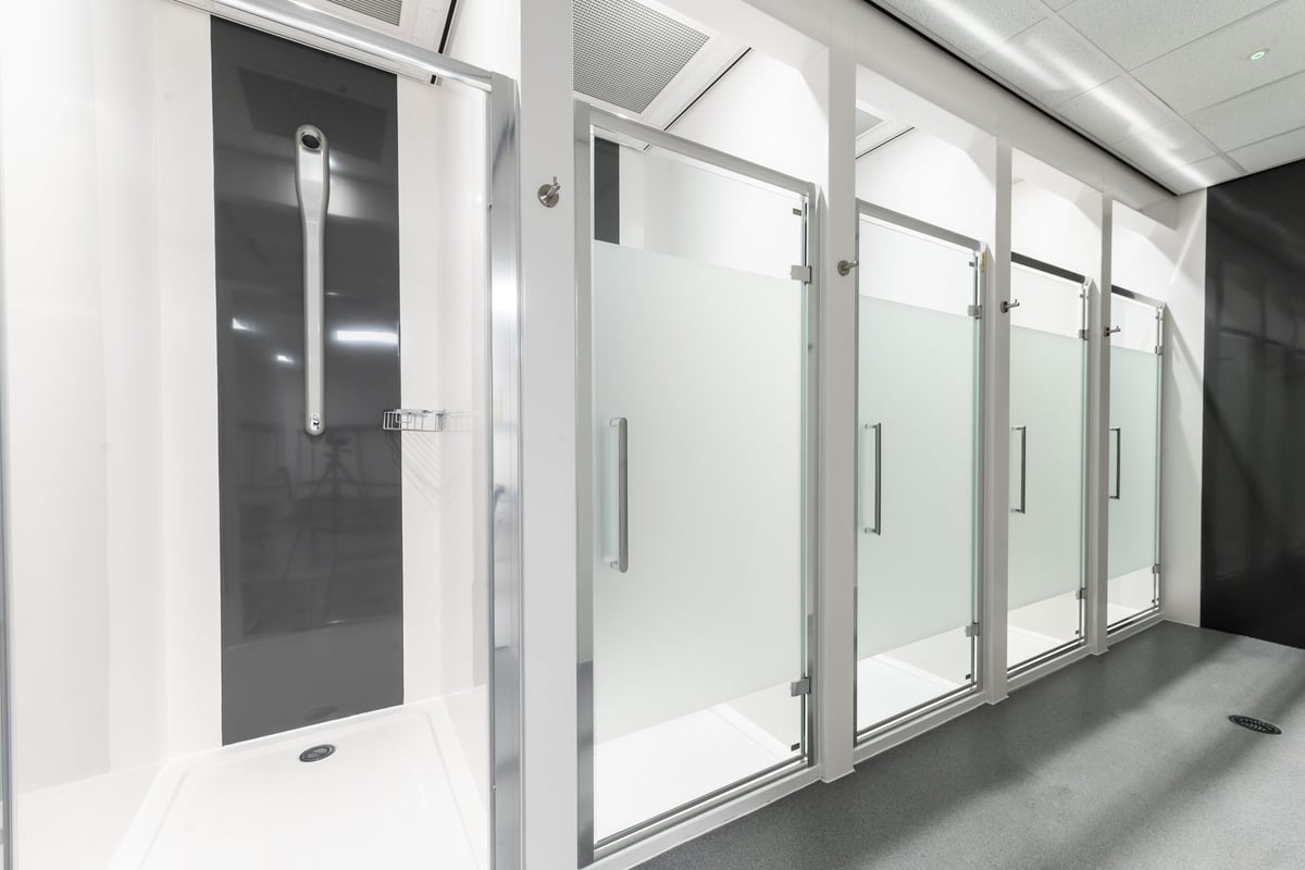 PureGym Peterborough Brotherhood Retail Park: Rows of glass-enclosed shower cubicles or changing rooms with door handles.