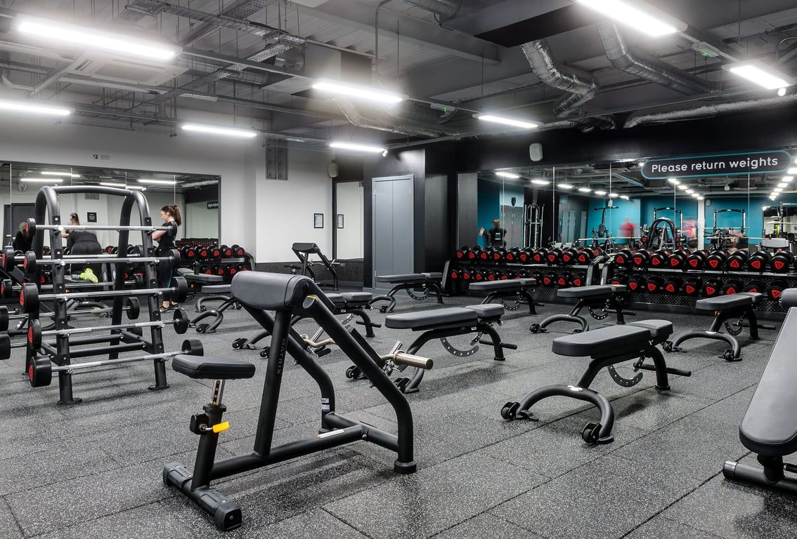 PureGym Glasgow Hope Street: Benches, weight racks, dumbbells, and rubberized flooring in a dimly lit fitness studio space.