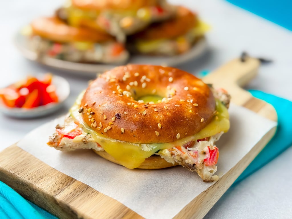 Sesame bagel sandwich with melted cheese and chicken on a wooden board