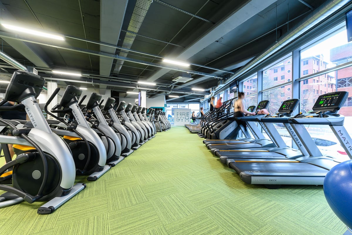 PureGym Leeds City Centre North: Rows of treadmills, exercise bikes and green flooring in a brightly lit gym interior.