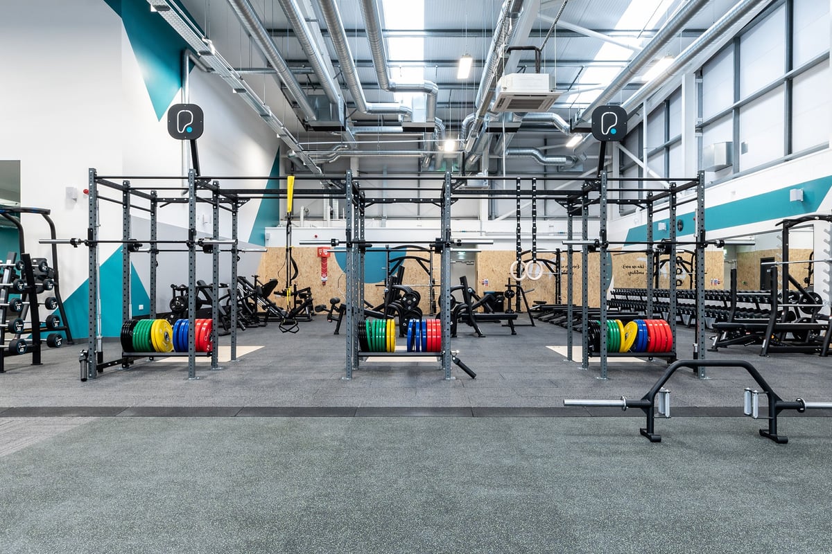 PureGym Blyth: Rig frames, weight plates in various colours, benches, and rubberised floor tiles.