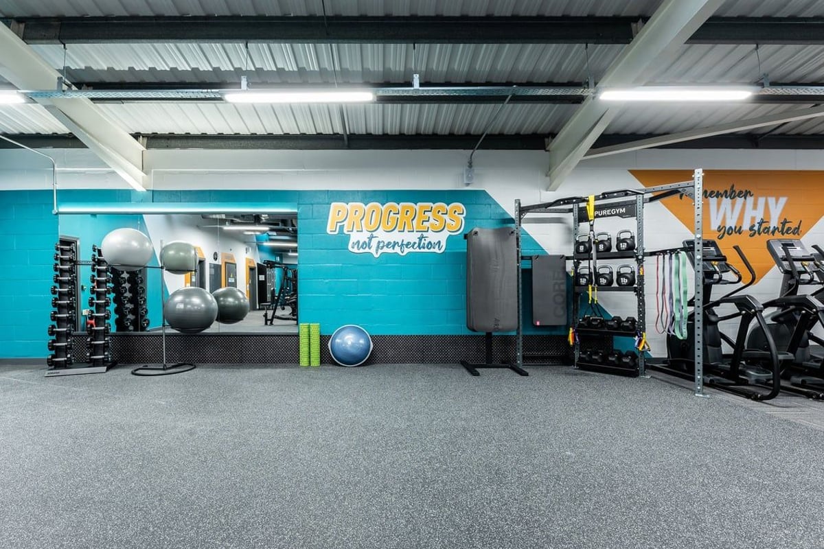 PureGym Boston: Strength training area with weight racks, medicine balls, squat racks, and rubberized flooring.