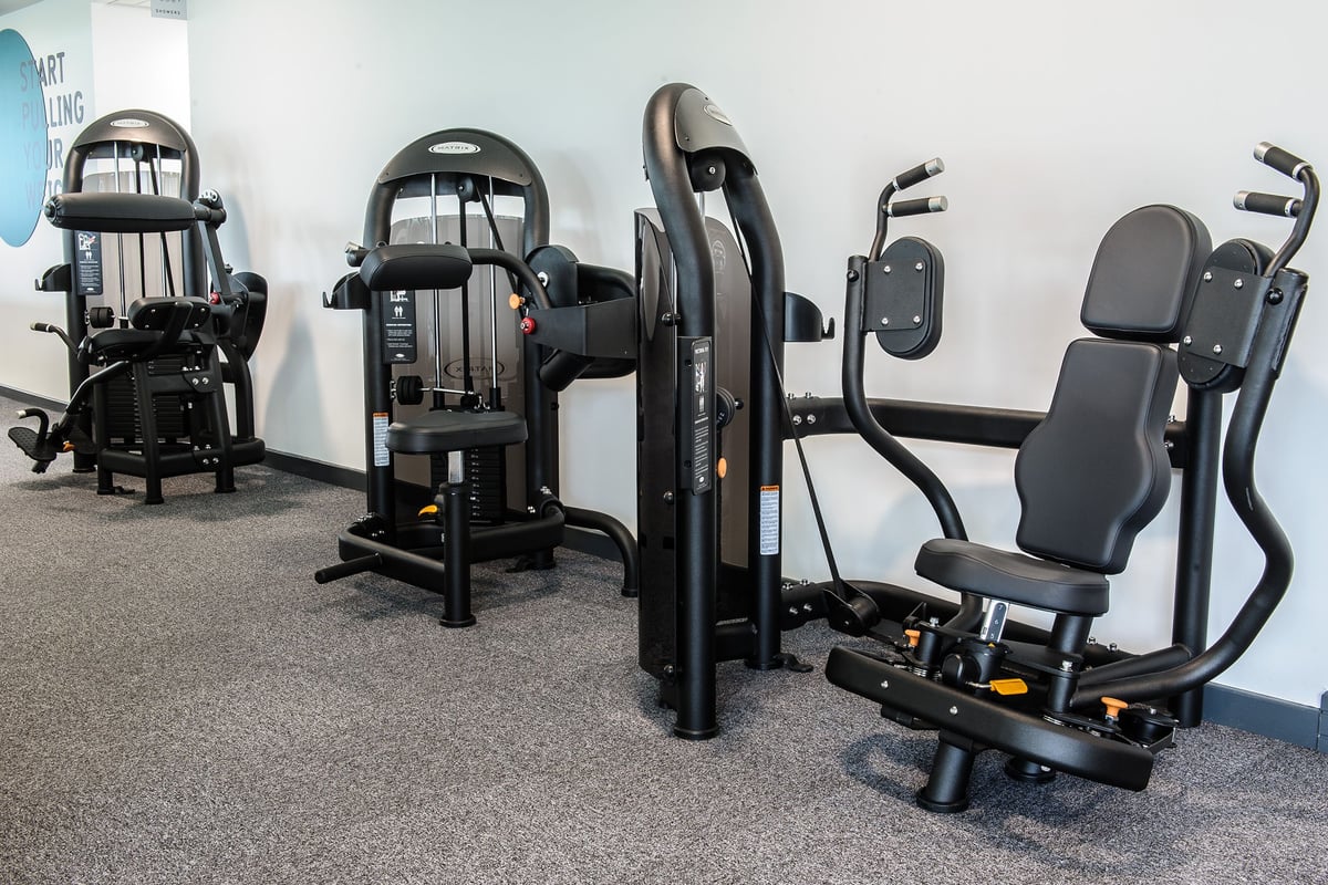 PureGym Denton: Weight machines, adjustment pulleys, padded seats for strength training in a gym setup.