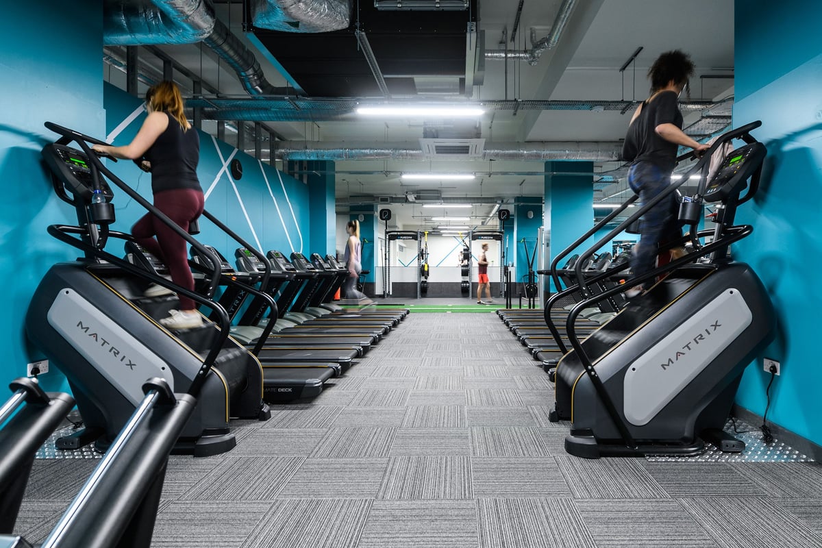 PureGym London Whitechapel: Rows of modern elliptical machines and treadmills in a futuristic blue-lit gym interior.