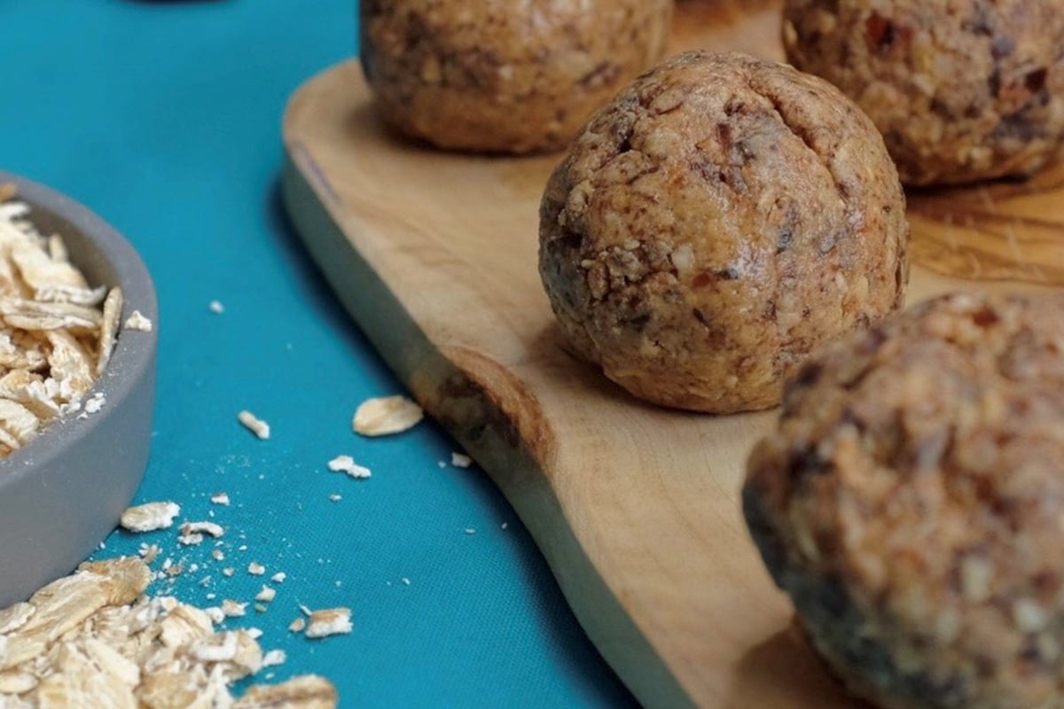 Energy balls on a wooden board with oats and dates on a blue surface nearby