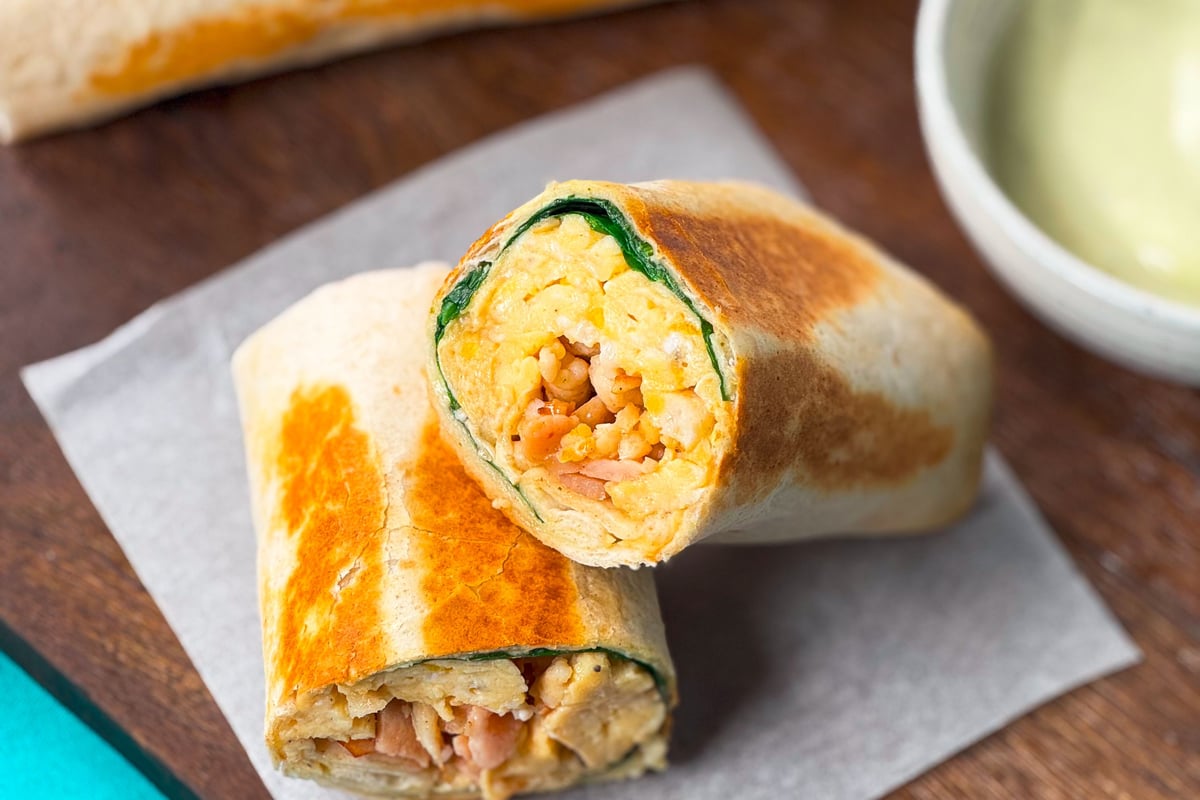 Grilled breakfast wrap cut in half showing scrambled eggs, spinach, and bacon inside.