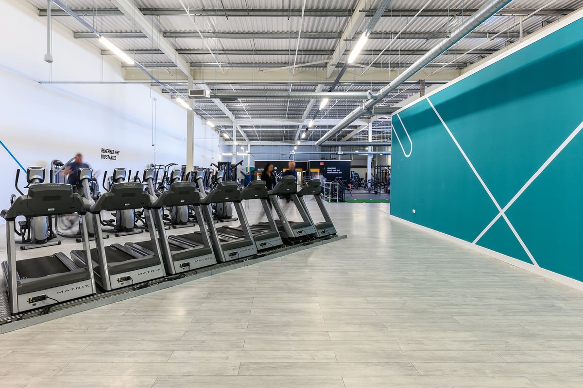 PureGym Wisbech: Rows of treadmills alongside teal partitions in a bright fitness centre interior.