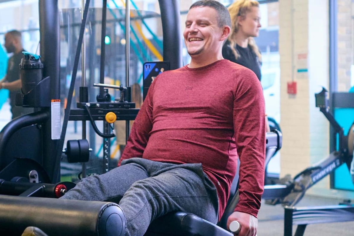 Man in red top exercising legs on gym machine while smiling