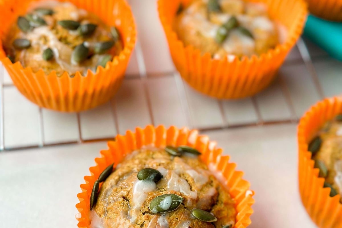 Pumpkin muffins with glaze and pumpkin seeds in orange paper cases on a cooling rack.