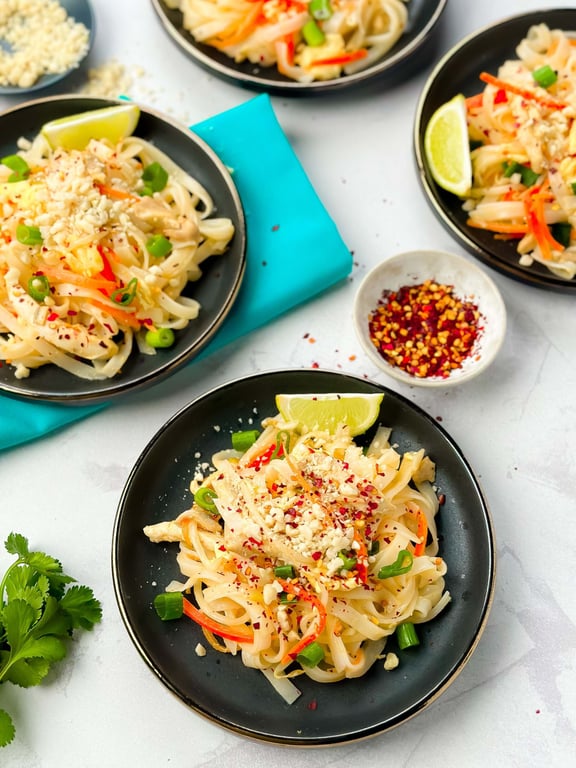 Black plates with noodle salad garnished with lime wedges, peanuts, and spring onions
