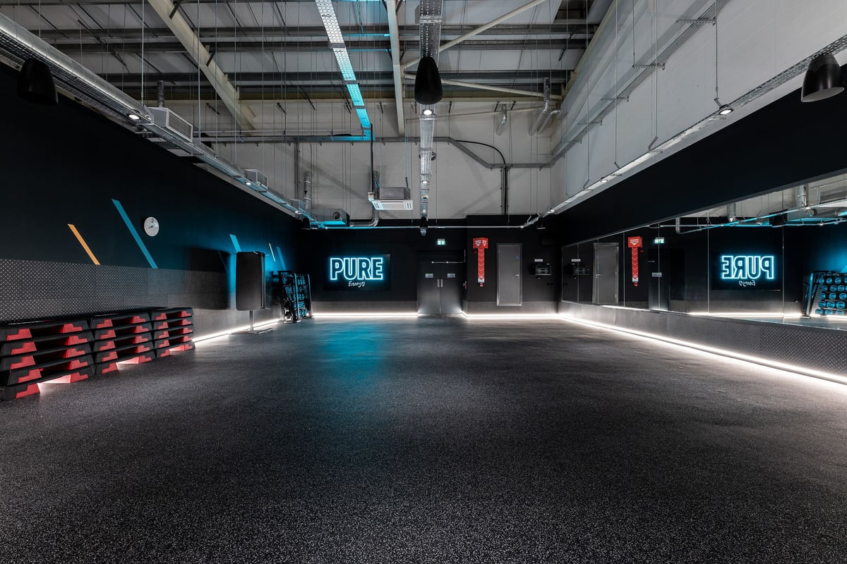 PureGym Lincoln Carlton Centre: Studio with red benches, mirrored walls, neon signage, and industrial ceiling.