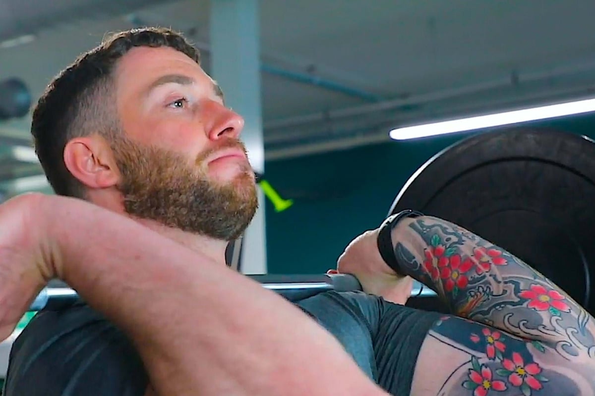 Man with tattoo lifting barbell in gym with focused expression