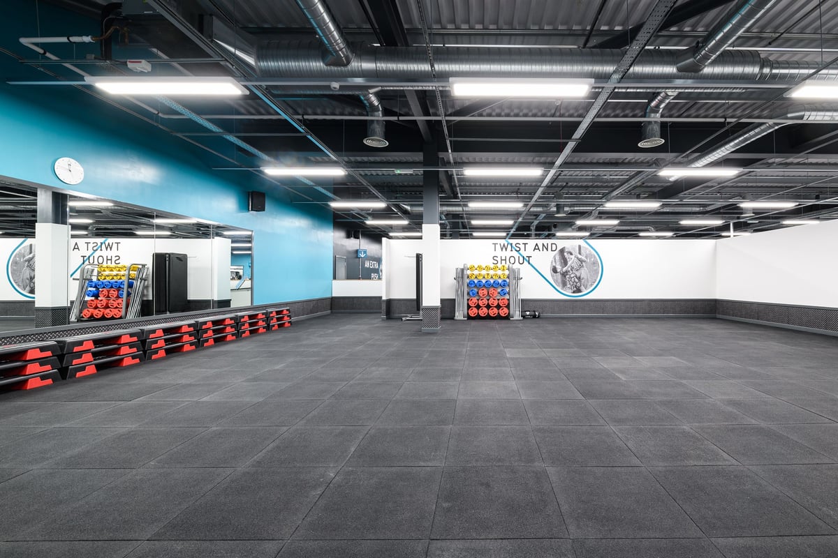 PureGym Newry: Rows of colourful weight plates, floor mats, fitness wall art, and ceiling-mounted lighting.