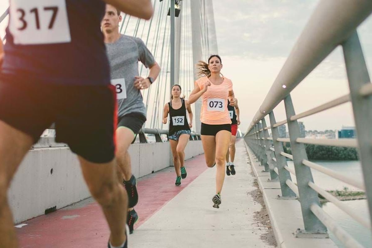 Runners with numbered bibs competing on a bridge during a race.