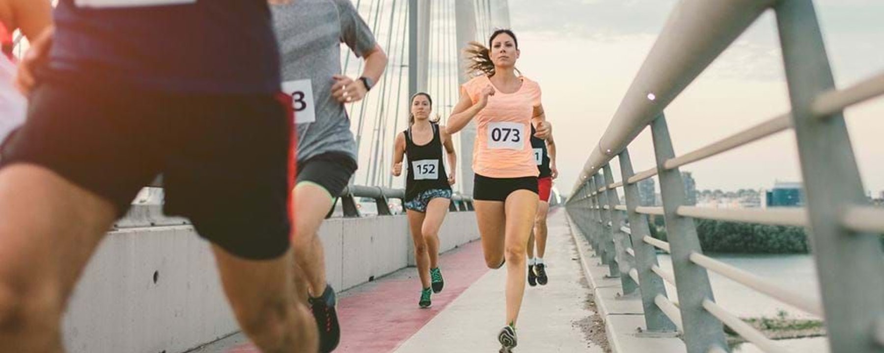 Runners with numbered bibs competing on a bridge during a race.