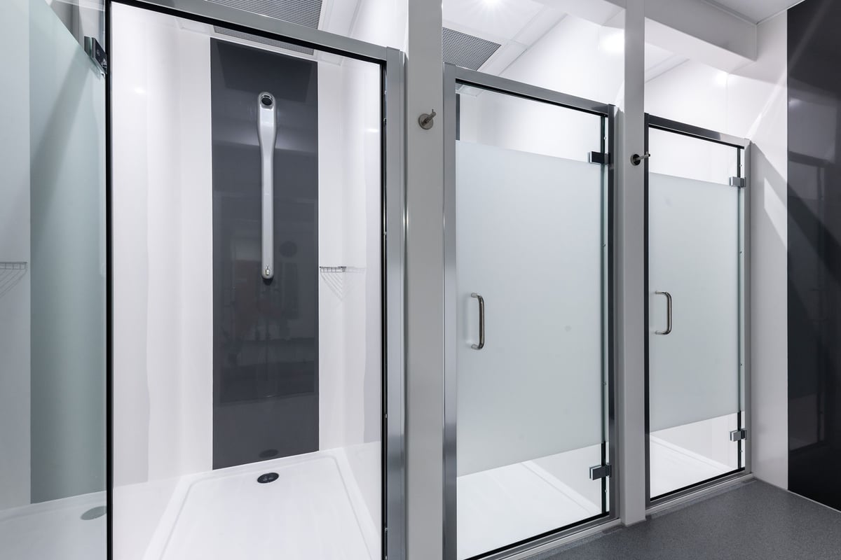 PureGym Caerphilly: Glass shower stalls, metal frames, and tiled flooring in changing room area.