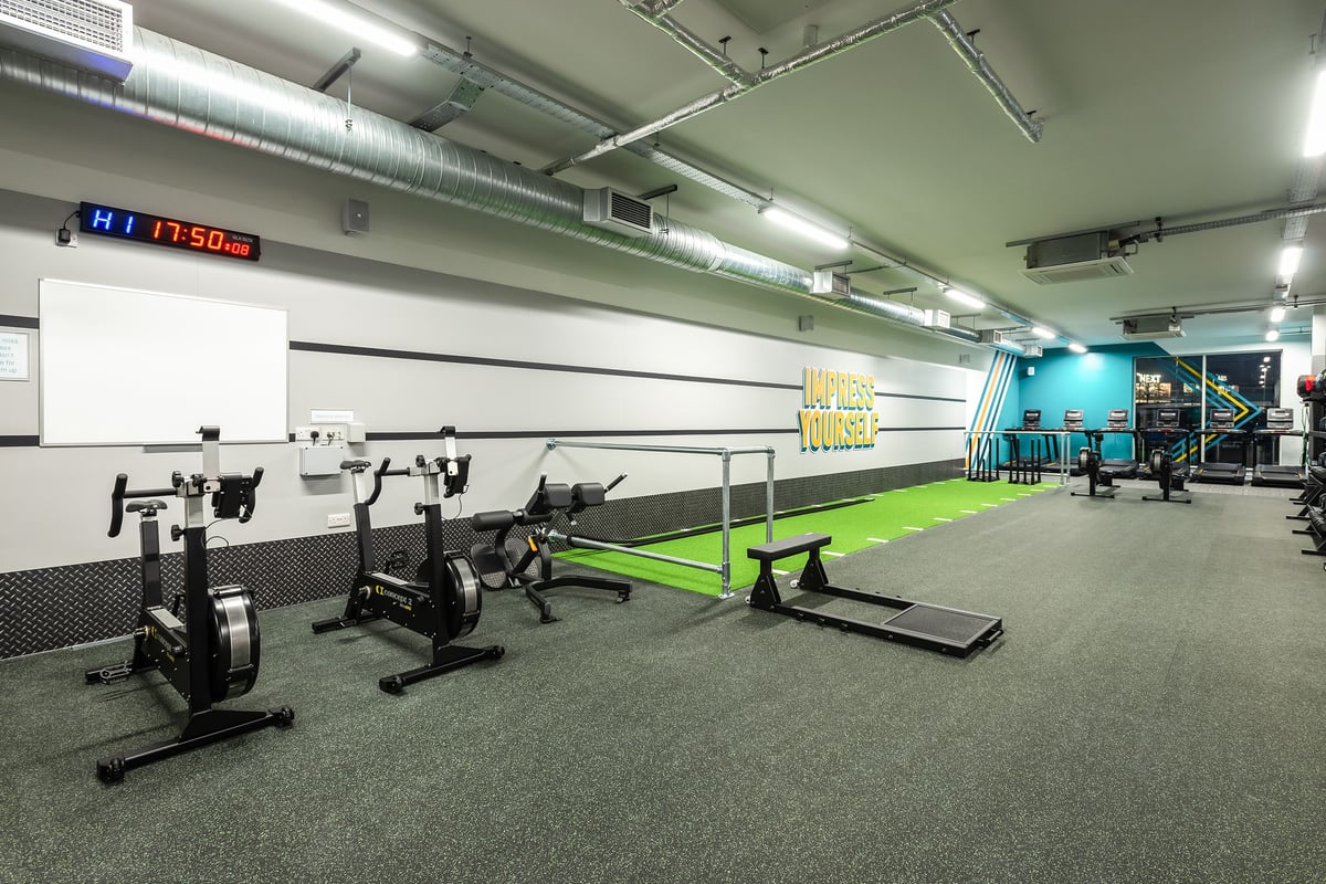 PureGym Llantrisant: Rows of indoor rowers, treadmills, weight racks, and rubberised flooring in a gym.