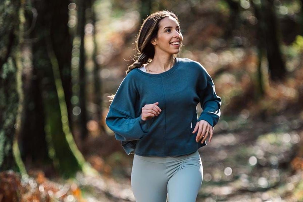 Woman in blue top jogging on a forest trail with autumn foliage in the background