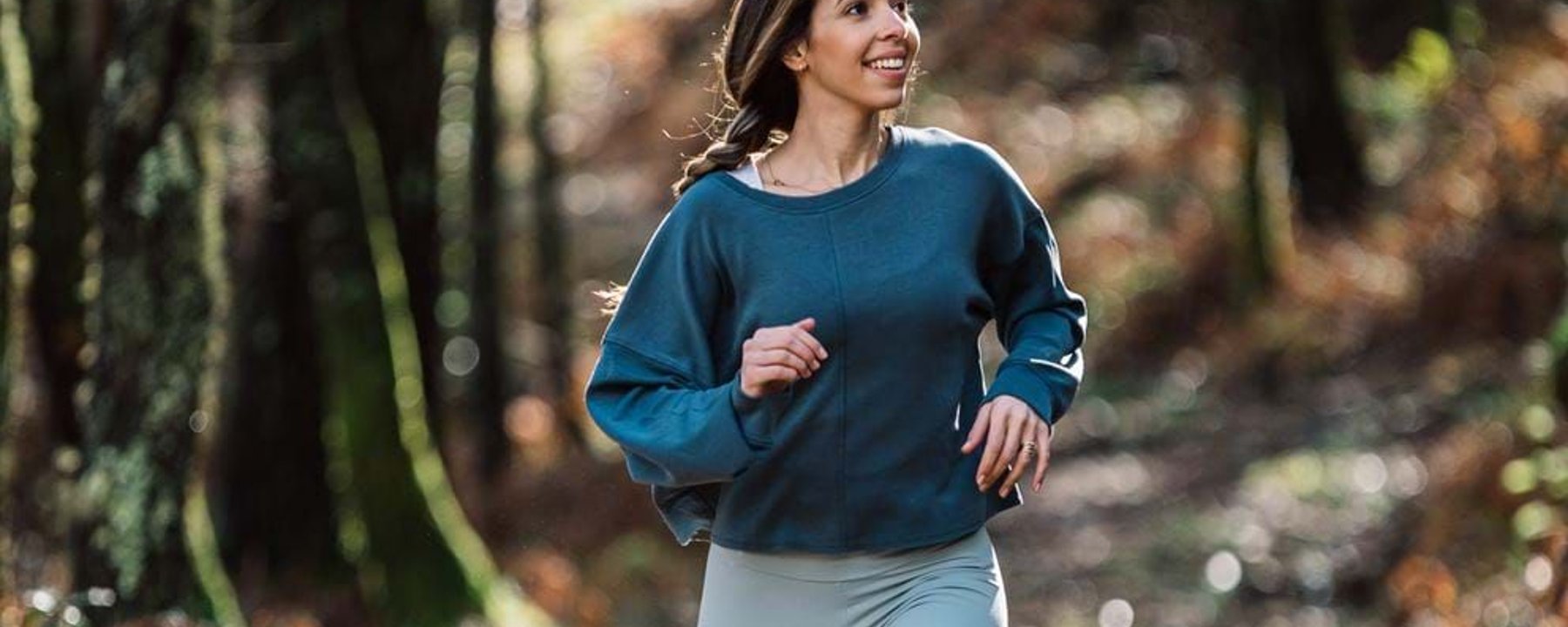 Woman in blue top jogging on a forest trail with autumn foliage in the background