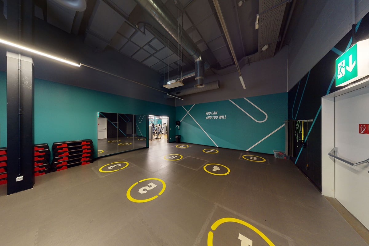 PureGym Winterthur Töss: Plancher avec cercles jaunes, bancs, murs bleu sarcelle, panneaux de sortie - espace de studio d'entraînement fonctionnel.