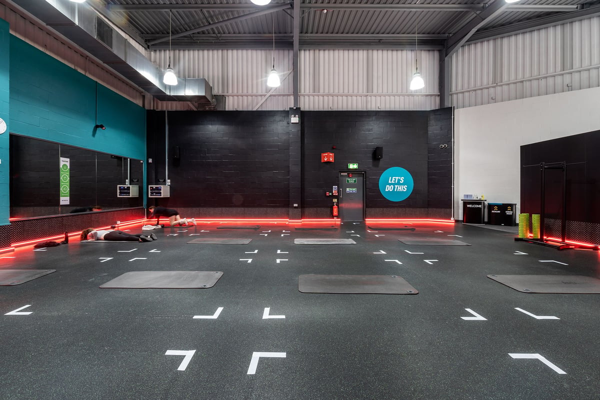 PureGym Warrington Central: Fitness studio with padded red floor mats, lifting platforms and weight racks.
