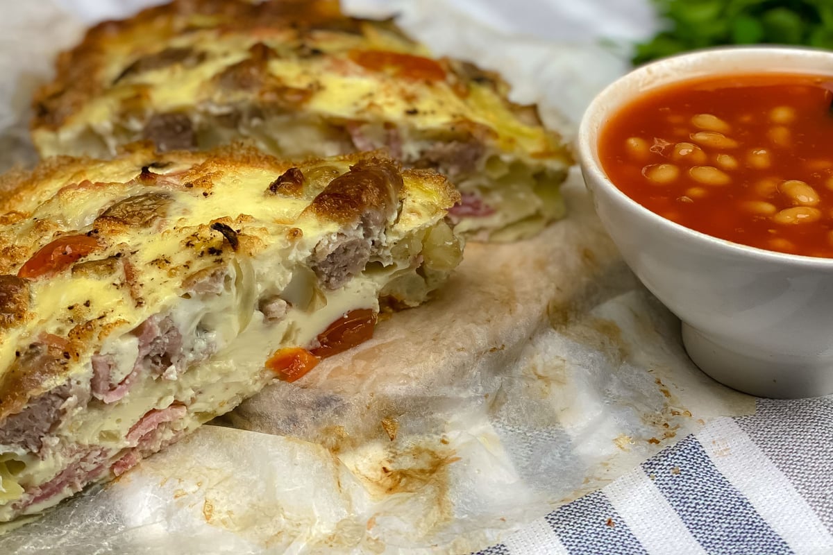 Sliced frittata with meat and cheese filling served with bowl of baked beans