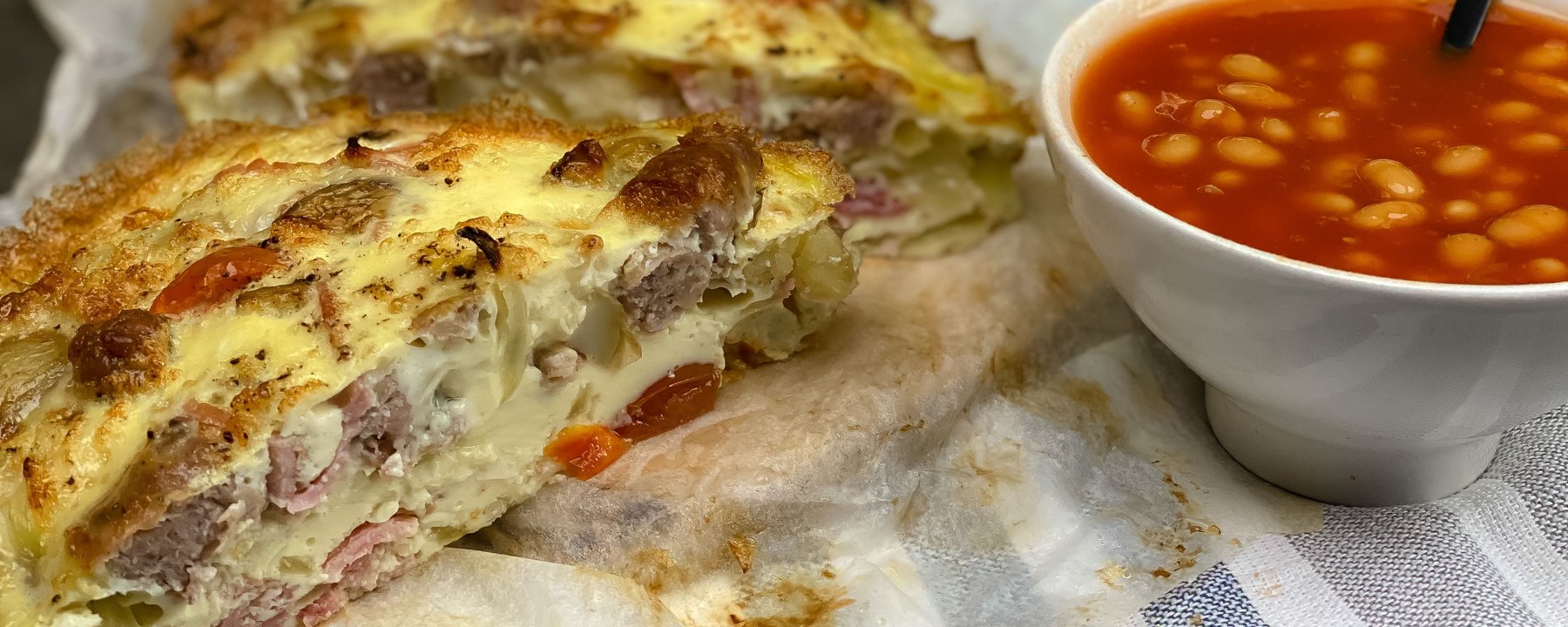 Sliced frittata with meat and cheese filling served with bowl of baked beans
